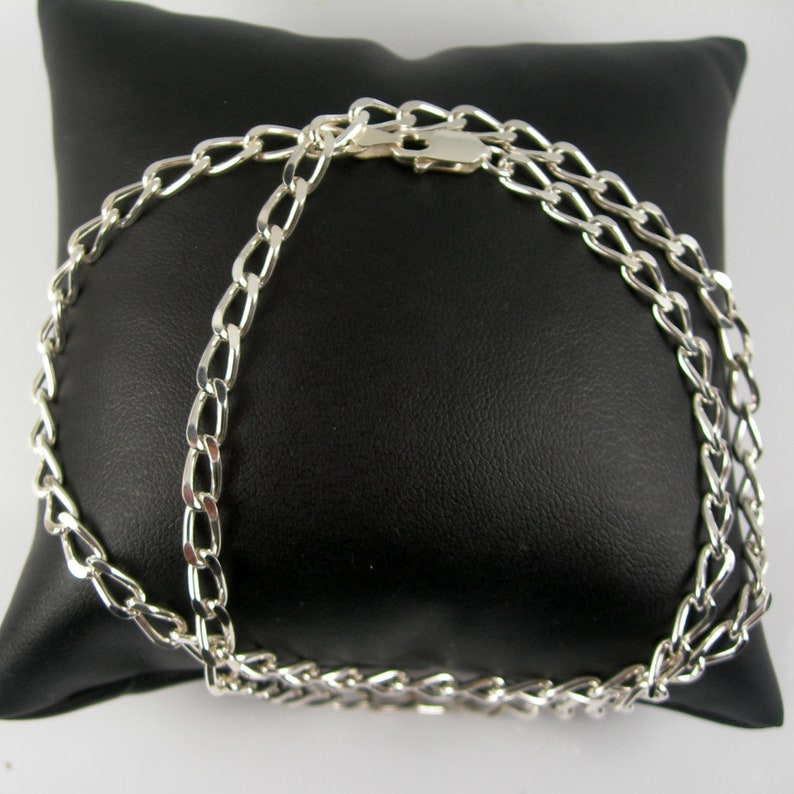 May include: A silver chain necklace with a curb link design. The chain is on a black velvet pillow.