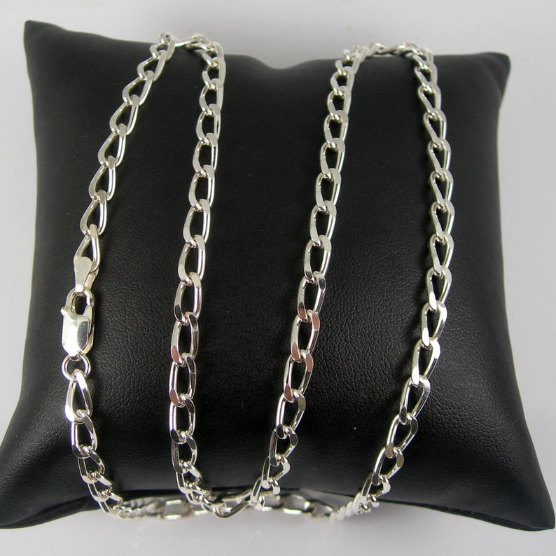 May include: A silver chain necklace with a curb link style. The chain is laying on a black velvet pillow.