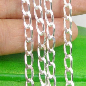 May include: Three silver curb chains of different lengths, laid out on a green surface.