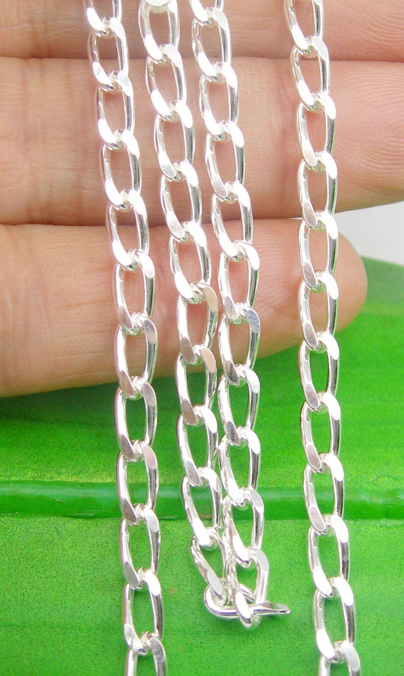May include: Three silver curb chains of different lengths, laid out on a green surface.