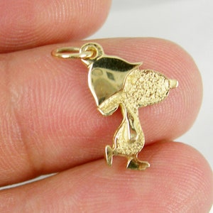 May include: A gold-colored charm in the shape of a cartoon character, featuring a textured body and smooth head and feet. The charm has a small loop at the top for attachment to a necklace or bracelet. The charm is approximately 0.75 inches in height.