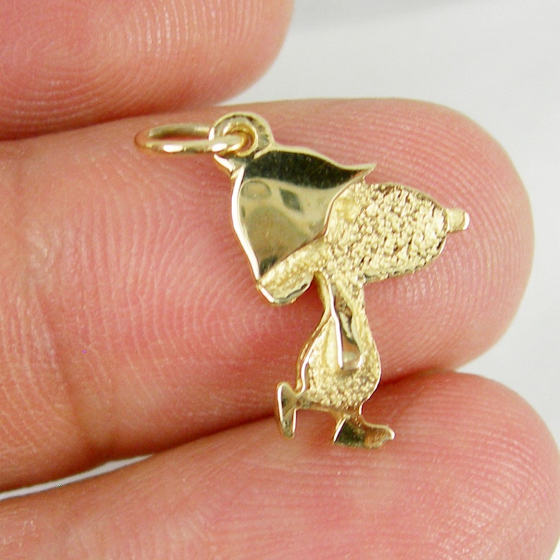 May include: A gold-colored charm in the shape of a cartoon character, featuring a textured body and smooth head and feet. The charm has a small loop at the top for attachment to a necklace or bracelet. The charm is approximately 0.75 inches in height.