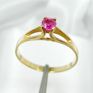 May include: A gold ring with a pink gemstone set in the center. The ring has a simple, elegant design with a delicate band.