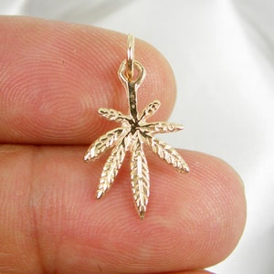 May include: A gold-colored marijuana leaf charm pendant. The charm is detailed with a textured design and has a loop at the top for attaching to a chain or bracelet.