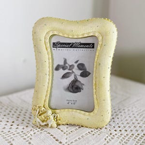 May include: A pale yellow photo frame with a decorative floral accent. The frame is embellished with small, sparkling beads. The photo size is 4" x 6". The text "Special Moments Memories Collection" is visible.