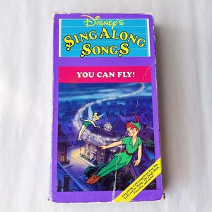 May include: A vintage VHS tape of Disney's Sing Along Songs, featuring Peter Pan and Tinkerbell. The cover is purple, with the title in yellow and the phrase "YOU CAN FLY!" in pink. The tape includes songs from Peter Pan, Lady and the Tramp, and more.