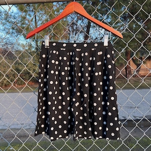 May include: A black and white polka dot skirt with a high waist and a pleated design.