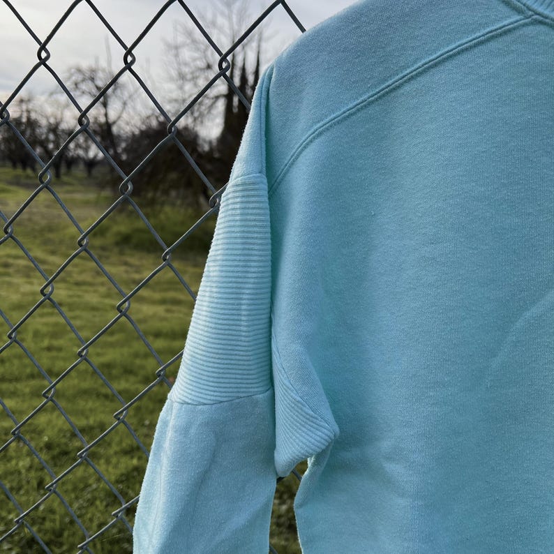 May include: A light blue sweatshirt with ribbed cuffs and a slightly textured fabric.