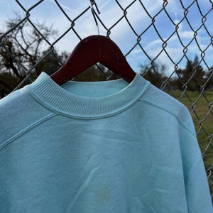 May include: A light blue sweatshirt with a ribbed crew neck.