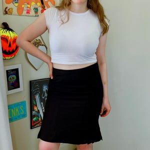May include: A white short-sleeved crop top paired with a black knee-length skirt. The skirt features a vertical ribbed texture and a slightly flared hemline. The top is a simple crew neck style, while the skirt sits at the natural waistline.