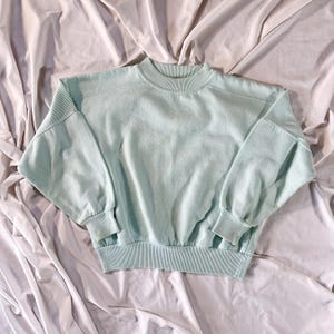 May include: A light green crew neck sweatshirt with long sleeves and a ribbed hem.