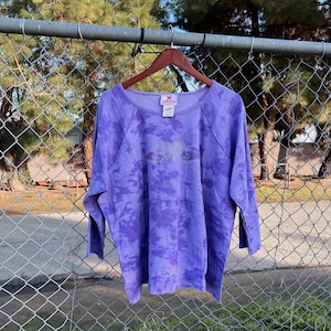 May include: Purple tie-dye sweatshirt with a rhinestone heart design. The sweatshirt has a crew neck and 3/4 sleeves.