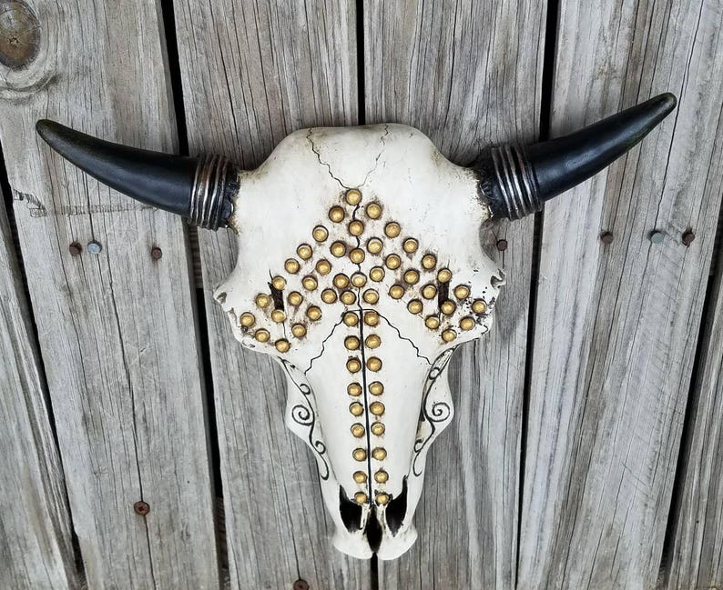 Peut inclure: Cr&acirc;ne de taureau blanc avec des clous dor&eacute;s et des cornes noires. Le cr&acirc;ne est d&eacute;cor&eacute; d'un motif noir et blanc.