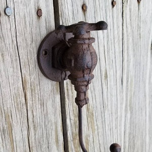 May include: A rustic cast iron wall hook shaped like a vintage water faucet with a decorative handle. The hook is painted in a dark brown color and has a weathered finish.