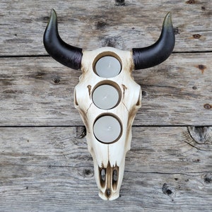 May include: White ceramic bull skull candle holder with three candle openings. The horns are black with green tips.