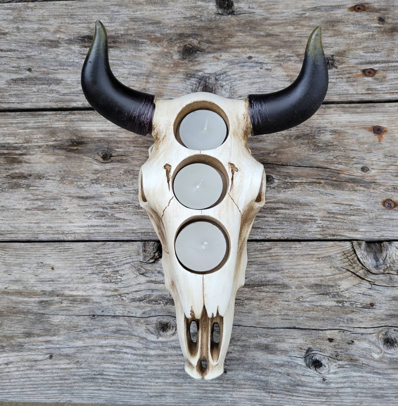 May include: White ceramic bull skull candle holder with three candle openings. The horns are black with green tips.