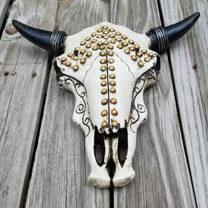 Peut inclure: Cr&acirc;ne de taureau blanc avec des cornes noires et des clous dor&eacute;s. Le cr&acirc;ne est d&eacute;cor&eacute; d'un motif noir et blanc.