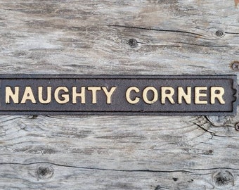May include: A black cast iron sign with gold lettering that reads "NAUGHTY CORNER".