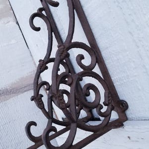 Puede incluir: Un par de soportes de estante de hierro fundido ornamentados con un dise&ntilde;o de desplazamiento. Los soportes son de color marr&oacute;n oscuro y tienen un acabado r&uacute;stico.