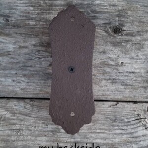 May include: A brown, decorative metal plate with a textured surface. The plate has a decorative top edge and is attached with a screw. The text "my backside" is written at the bottom.