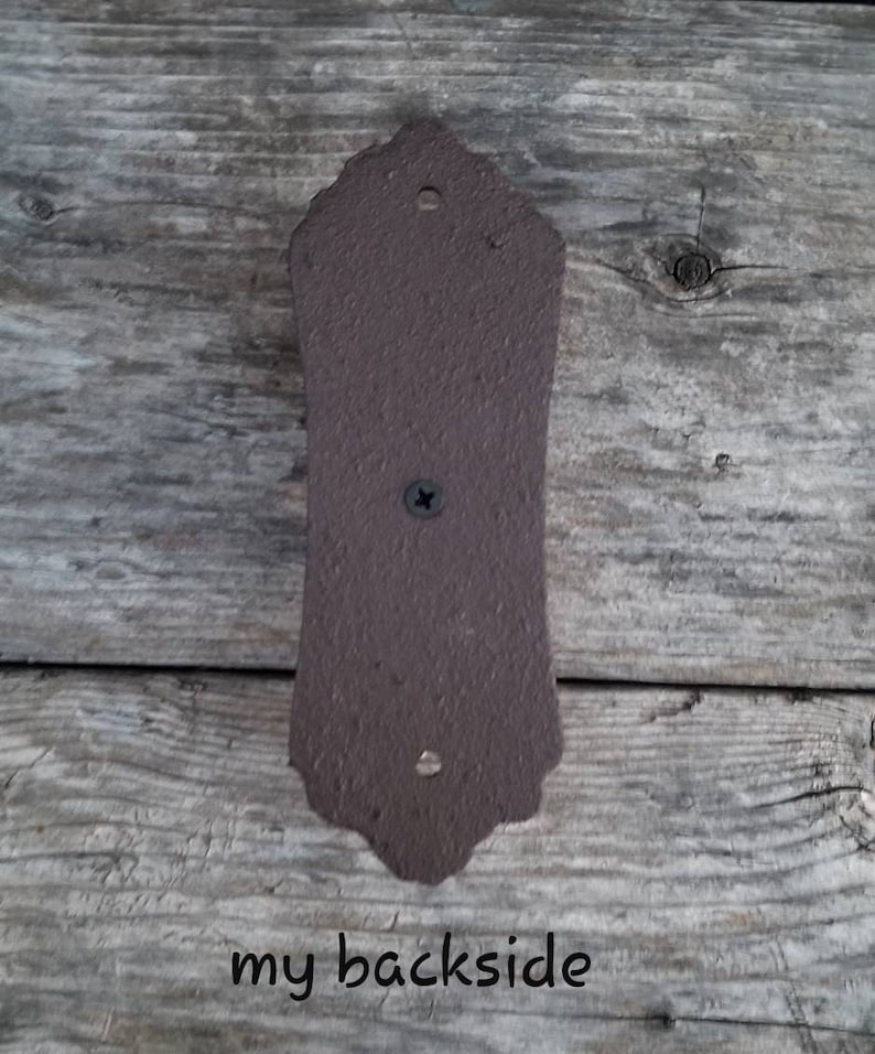 May include: A brown, decorative metal plate with a textured surface. The plate has a decorative top edge and is attached with a screw. The text "my backside" is written at the bottom.