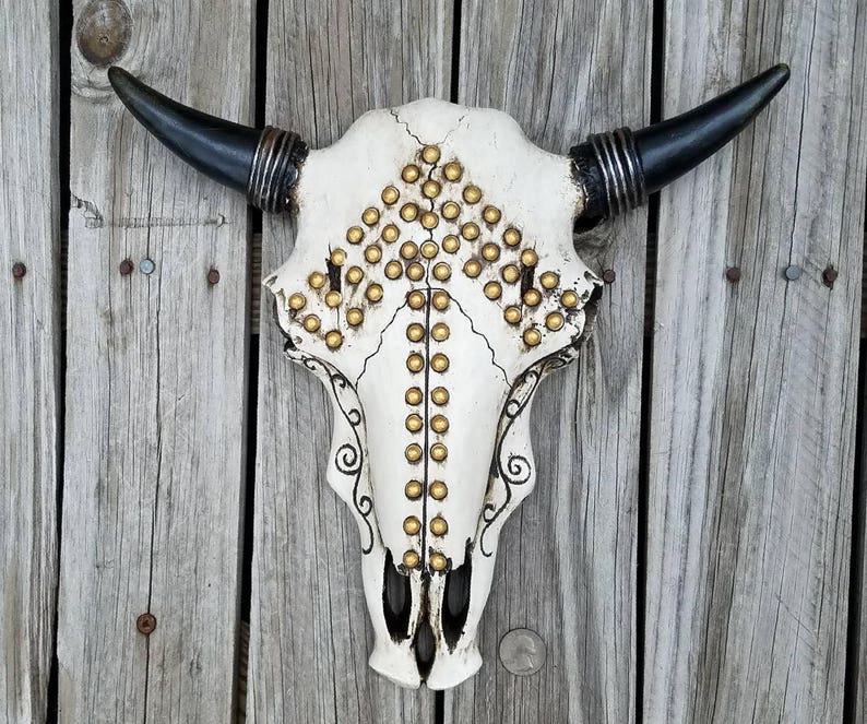 Peut inclure: Cr&acirc;ne de taureau blanc avec des clous dor&eacute;s et des cornes noires mont&eacute; sur un mur en bois.