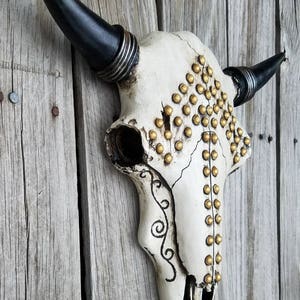 Peut inclure: Cr&acirc;ne de taureau blanc avec des cornes noires et des clous dor&eacute;s. Le cr&acirc;ne a un motif d&eacute;coratif sur le c&ocirc;t&eacute;.