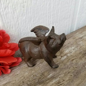 K&ouml;nnte beinhalten: Eine Schweinefigur aus Gusseisen mit Fl&uuml;geln. Das Schwein ist braun und hat ein detailliertes Gesicht. Die Fl&uuml;gel sind ausgebreitet und ebenfalls aus Gusseisen.