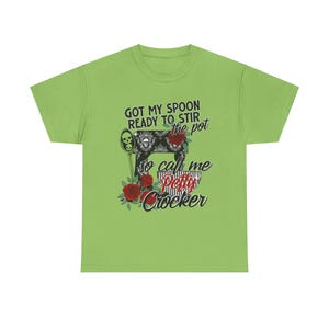 Peut inclure: T-shirt vert avec une illustration noir et blanc d'un batteur sur socle avec des roses rouges et le texte "Got my spoon ready to stir the pot so call me Petty Crocker".