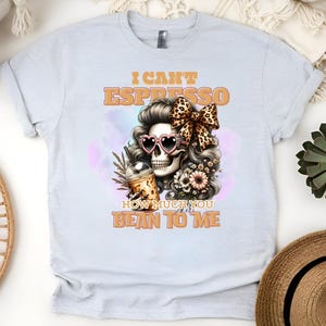 Op de afbeelding: Een lichtgrijs T-shirt met een schedel die een zonnebril en een bloemenkroon draagt. De tekst op het shirt luidt "I can't espresso how much you bean to me".