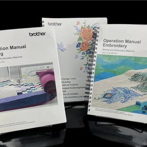 Op de afbeelding: Drie spiraalgebonden handleidingen met het "brother" logo. De handleidingen zijn getiteld "Operation Manual Sewing", "Design Guide" en "Operation Manual Embroidery". De naaihandleiding toont een naaimachine en een quilt. De borduurhandleiding toont een pauwenveermotief.