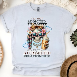 May include: White t-shirt featuring a colourful skull graphic and the text "I'm not addicted to coffee, we're just in a committed relationship."