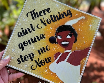 May include: A gold glitter background with a white pearl border. The image features a cartoon illustration of a woman with a microphone singing. The text "There ain't Nothing gonna stop me Now" is written in black lettering.