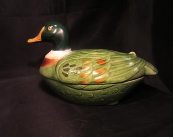 Könnte beinhalten: Eine grüne und braune Keramik-Servierplatte in Form einer Ente mit Deckel. Die Ente hat einen weißen Streifen um den Hals und orangefarbene Akzente an den Flügeln.