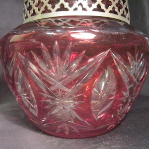 Puede incluir: Un cuenco de vidrio rojo rubí con un diseño de cristal tallado. El cuenco tiene un borde de metal plateado.