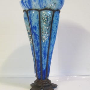 May include: A tall, decorative vase with a flared top and a dark, ornate base. The vase features a blue and white marbled design with vertical dark lines and silver accents. The base has a star-like shape.