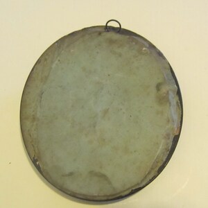 May include: The back of a round, framed, antique mirror with a light green backing. The frame is made of dark metal and has a small metal loop at the top for hanging.