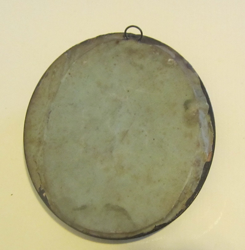 May include: The back of a round, framed, antique mirror with a light green backing. The frame is made of dark metal and has a small metal loop at the top for hanging.