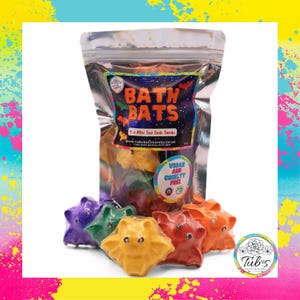 May include: A clear plastic pouch containing five bat-shaped bath bombs in purple, green, yellow, red, and orange. The label features the text BATH BATS, 5 x Mini Bat Bath Bombs, and a circular sticker stating VEGAN AND CRUELTY FREE.
