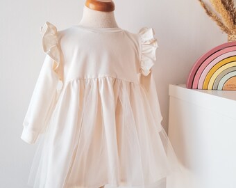 May include: A white tulle dress with long sleeves and a ruffled neckline. The dress has a gathered skirt and is made of a soft, comfortable fabric.