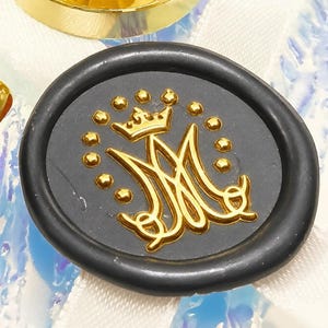 May include: Two gold-toned metal wax seal stamps with wooden handles and a circular black wax seal featuring a gold embossed monogram of the letter M topped with a crown and surrounded by a circle of small dots on a white ribbon.