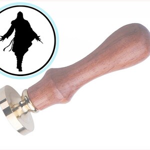 May include: A wax seal stamp with a wooden handle and a circular brass head featuring a silhouette of a hooded figure with outstretched arms.