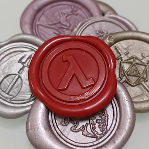 May include: A collection of six wax seals, each with a different design. The seals are in various colours, including red, silver, and gold. The red seal features the Lambda symbol, a stylized letter L, in a circle. The other seals feature various designs, including a sword, a dice, and a dragon.