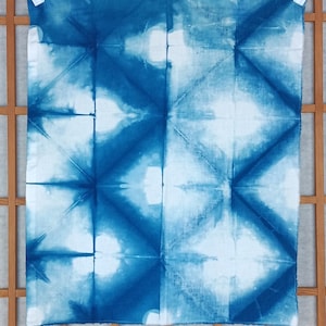 May include: A blue and white tie-dye fabric with a geometric pattern. The fabric is folded in half and hung on a clothesline.
