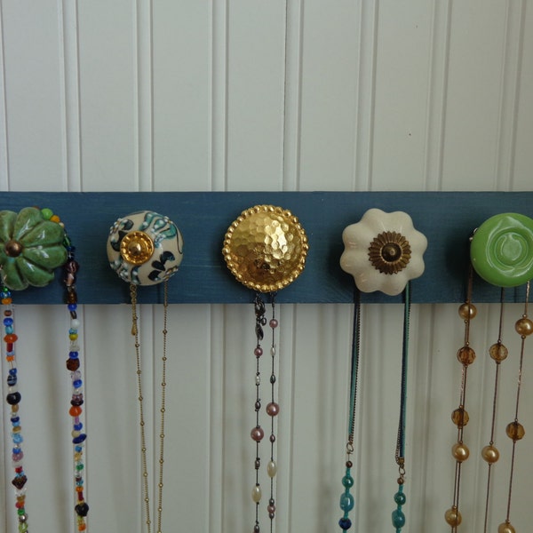 Beautiful dusty turquoise distressed wooden wall plaque with decorative knobs for organizing jewelry.