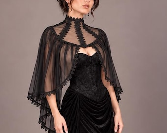 Puede incluir: Un vestido largo de terciopelo negro con escote corazón y corpiño ajustado. El vestido se combina con una capa de tul negro transparente que tiene un cuello alto de encaje y bordes festoneados, cayendo sobre los hombros y la parte superior de los brazos.