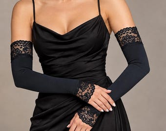 May include: A pair of black arm sleeves featuring intricate black lace trim at the upper arm and wrist openings. The sleeves are made of a solid black fabric and are worn with a matching black sleeveless dress with a cowl neckline.