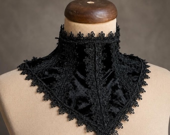 Può includere: Un girocollo in velluto nero con intricate rifiniture in pizzo lungo i bordi. L'accessorio a collo alto presenta un pannello frontale a punta a forma di V con dettagli in pizzo verticale e un bordo smerlato lungo tutta la scollatura.