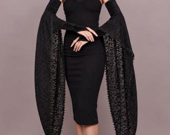May include: A black strapless midi dress paired with long, detached black lace sleeves. The sleeves feature a fitted upper section and wide, flared lower sections with scalloped edges. The dress has a simple, form-fitting silhouette.
