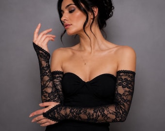 May include: A pair of black lace arm sleeves featuring a delicate floral pattern and scalloped edges. The sleeves extend from the upper arm down to the wrist, showcasing intricate needlework and a sheer, lightweight construction in black.